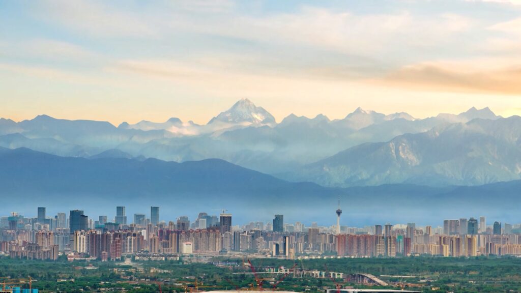 Chengdu skyline at golden hour with the snow-capped Siguniang range rising behind the city